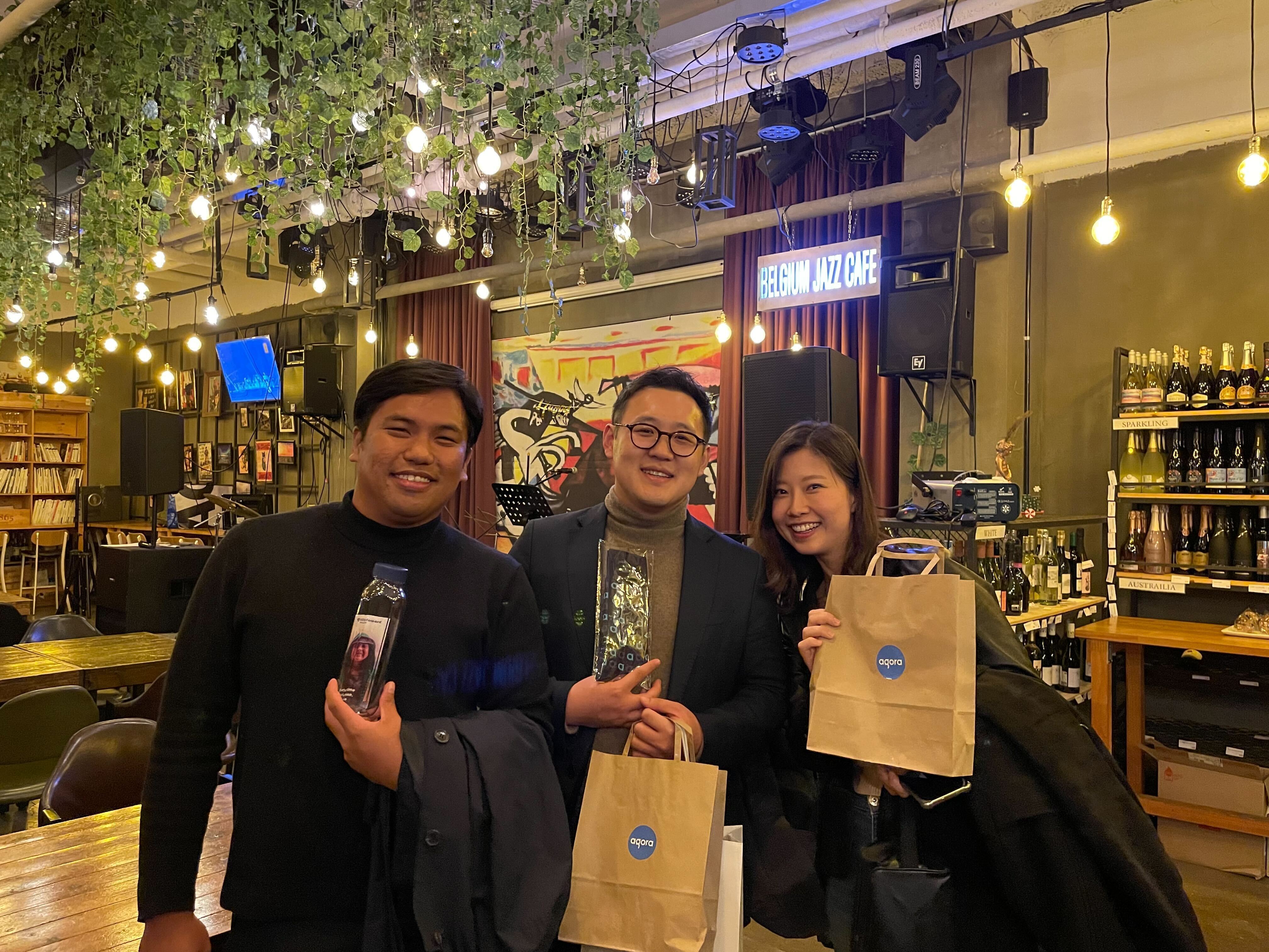 Three people smiling holding Agora gift bags in Seoul, South Korea