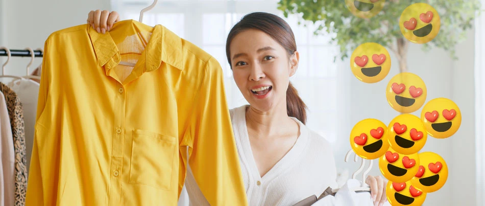 A person holds up a yellow shirt as smiling emojis with hearts for eyes display to their right.