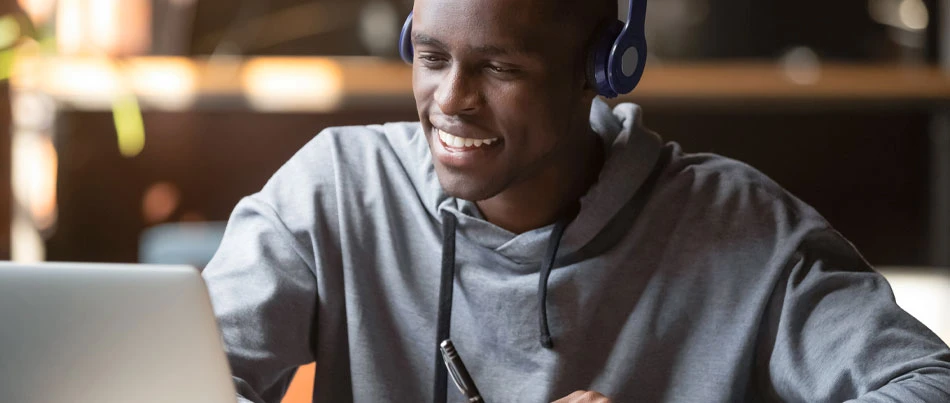A person wearing headphones smiles as they use a laptop.