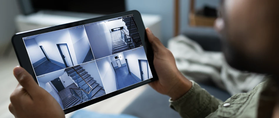 A man holding an ipad showing the security footage of 4 locations, to angles for the apartment hallway and two for the apartment stairwell