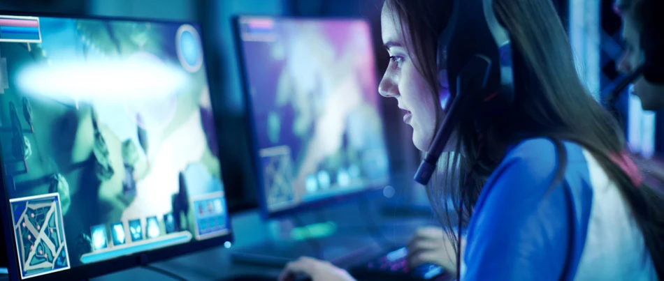 A person wearing headphones looks intently at their computer monitor while playing a video game.