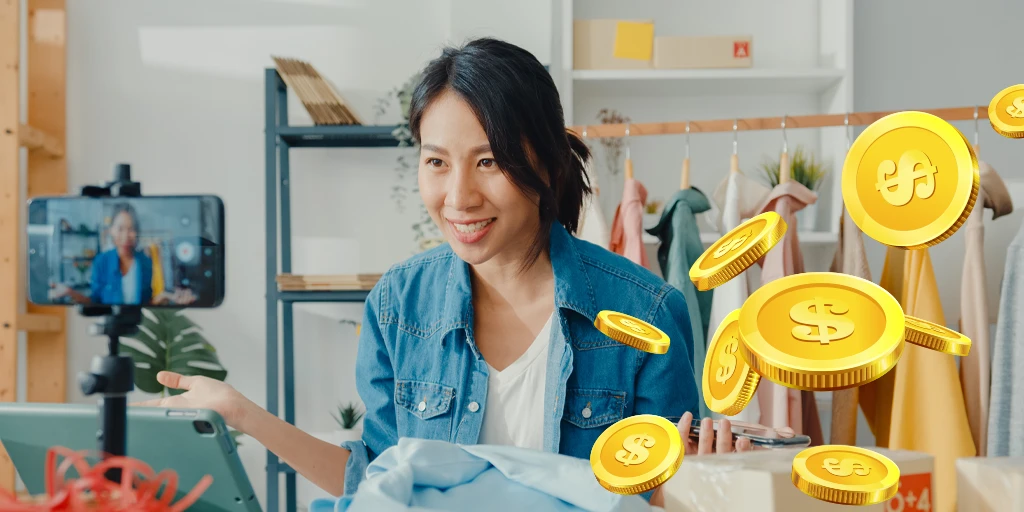 A woman in a blue jacket on live video call is surrounded by gold coins