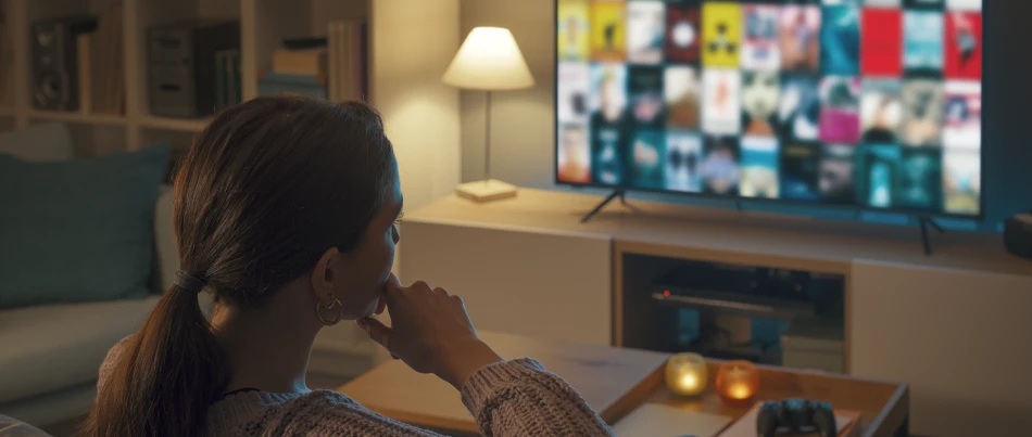 A woman at home sitting on the couch browsing movie selections on her smart tv